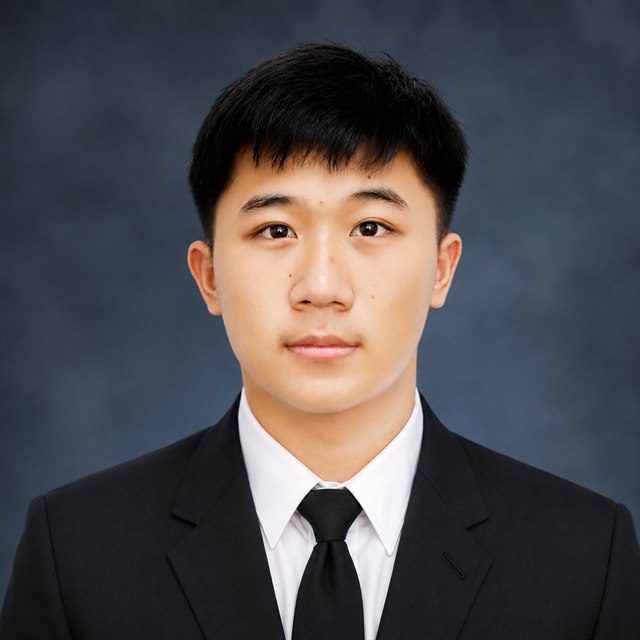 Chamroeun Hongleng — head-and-shoulders portrait, facing the camera in a dark suit, white shirt, and black tie against a grey studio backdrop.